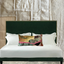 Bed with green headboard and decorative pillow against a textured wall.