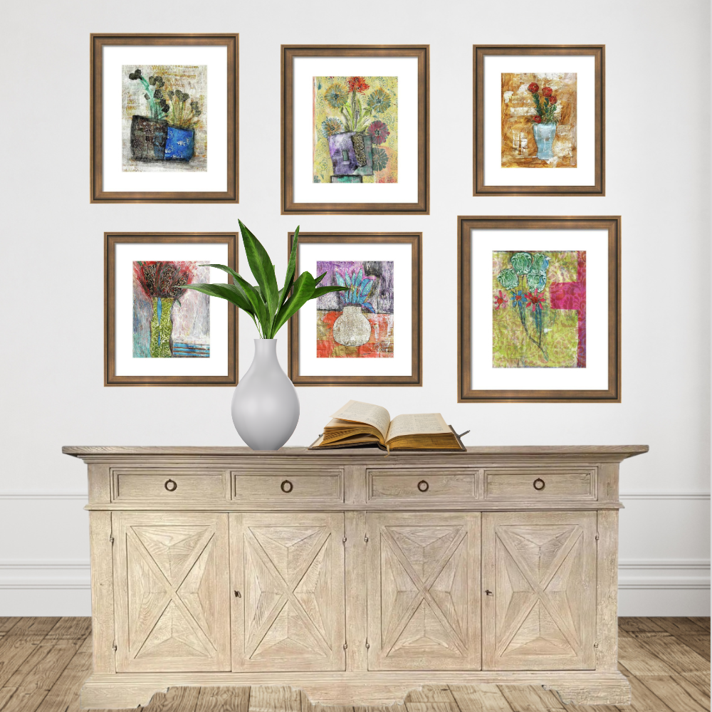 Framed artworks on a wall above a wooden sideboard with a vase and book.