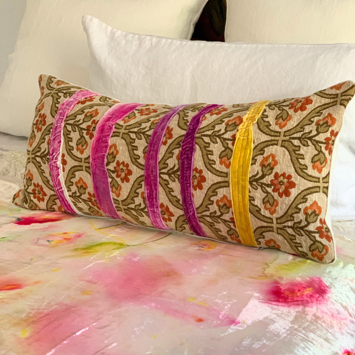 Decorative pillow with floral patterns and colorful stripes on a bed with a floral comforter.