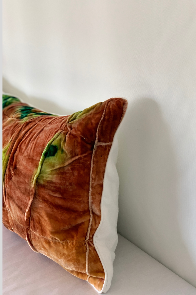 Brown and green patterned pillow on a white surface with a light gray background