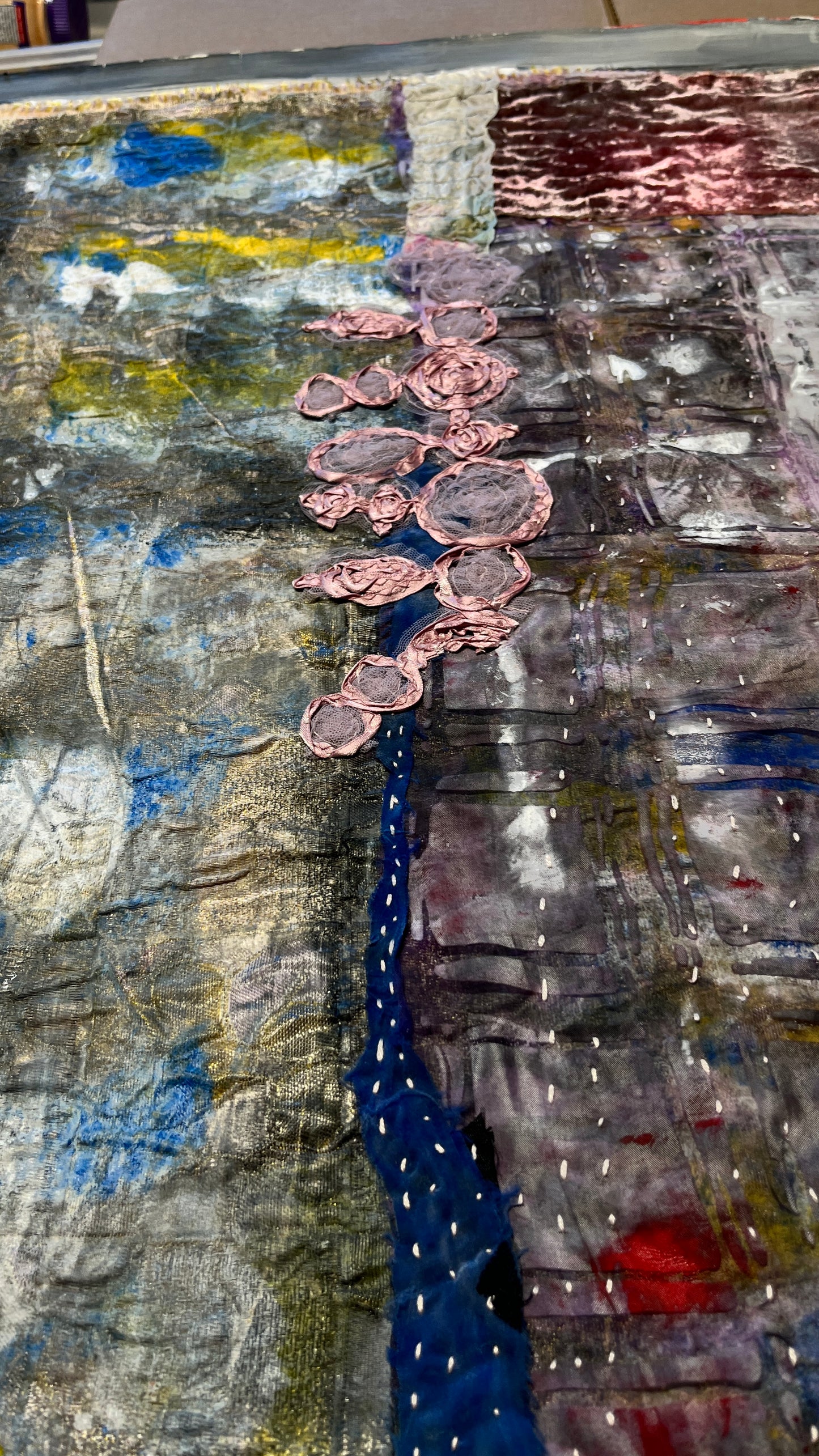 Work on progress of an riginal textile-on-paper abstract artwork featuring stitched pink textile elements, layered acrylic paint, collage, blue accents, and textured gray and burgundy surfaces.