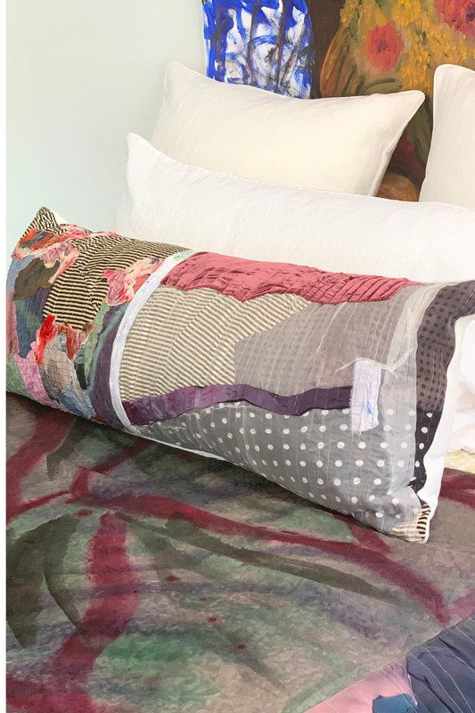Artistic decorative pillow for bedding featuring patchwork textures and vibrant fabrics on a white bed.