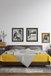 Bedroom with a bed, yellow blanket, and framed pictures on the wall.
