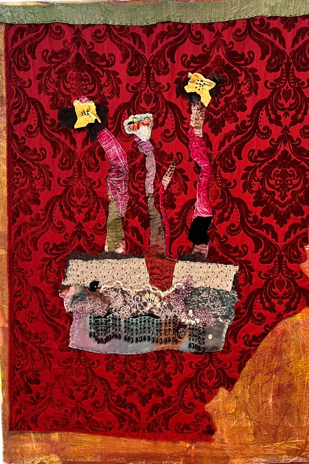 Textile art piece with abstract figures on a red patterned background