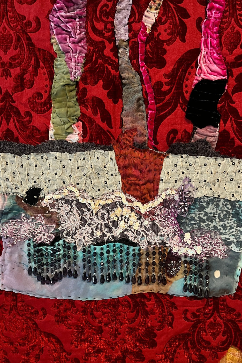 Textile art piece with colorful patterns and textures on a red background