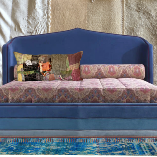 blue bed, with colorful cushions against a textured wall.