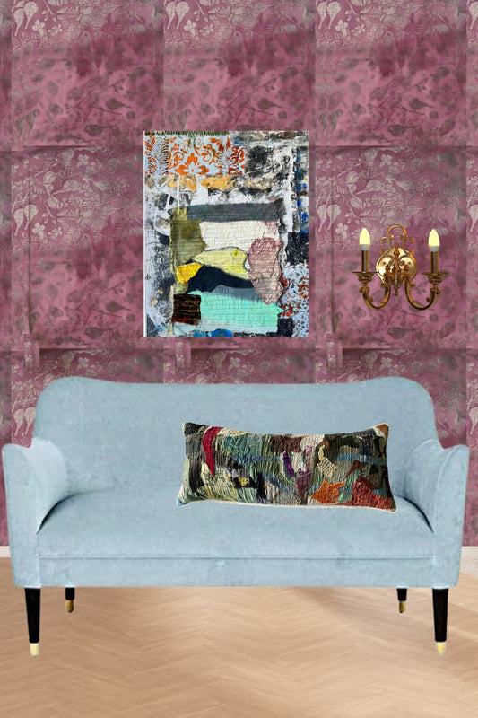 A light blue upholstered loveseat with a multicolor abstract patchwork lumbar pillow, set against a pink patterned paneled wall with a matching abstract canvas art piece and a gold wall sconce.