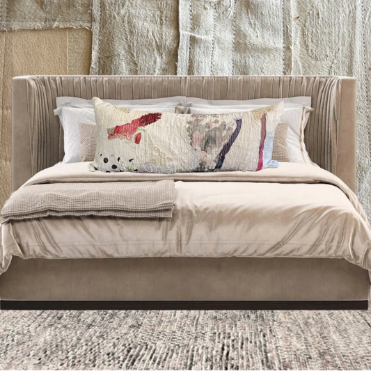 Beige upholstered bed with patterned pillows against a textured wall.