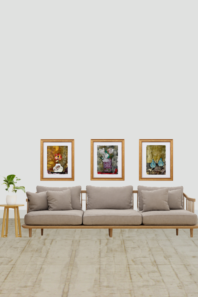 Beige sofa with wooden frame against a white wall with three framed artworks.