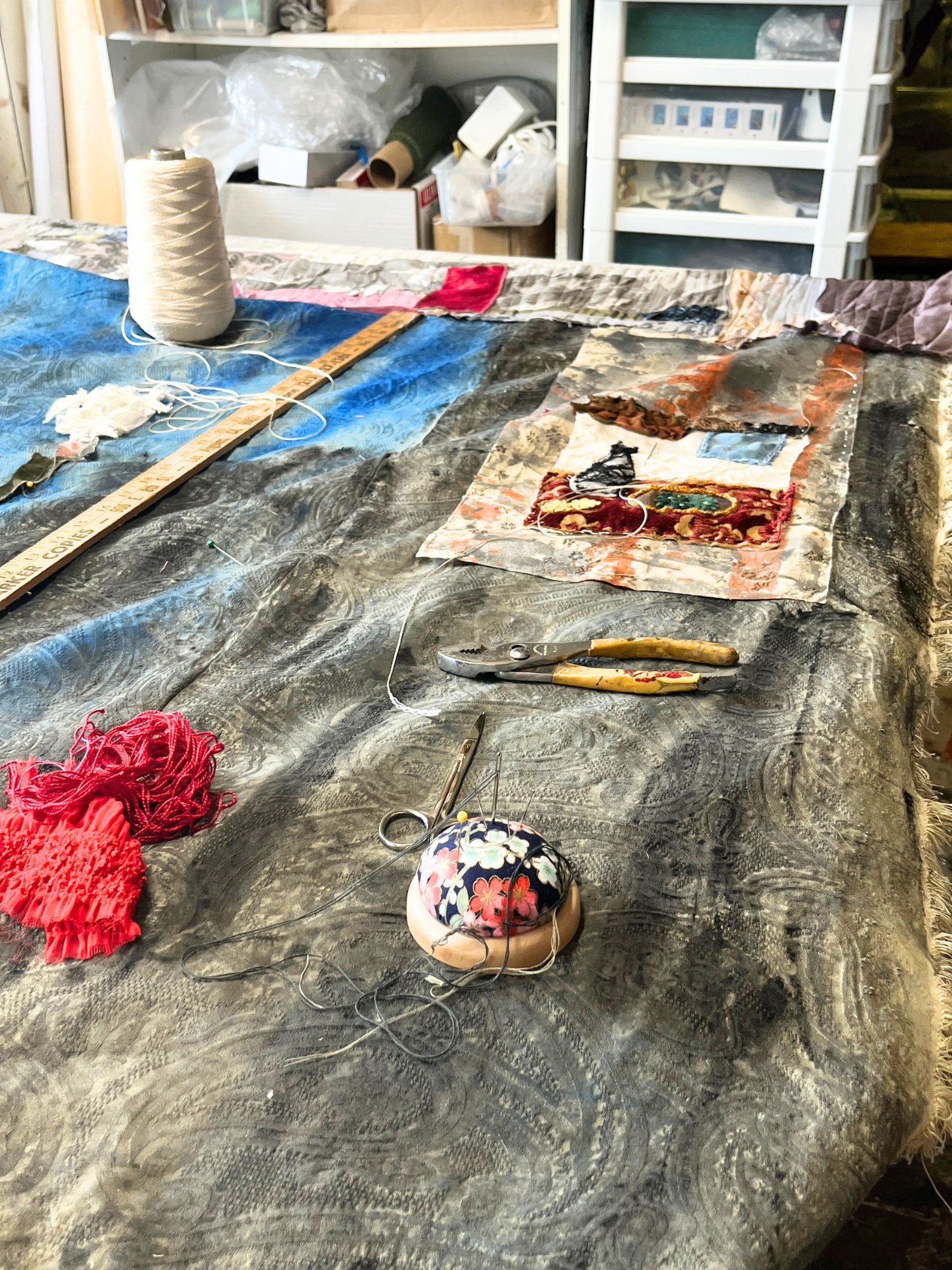 Artistic workspace with fabric pieces, yarn, and sewing tools on a wooden table.