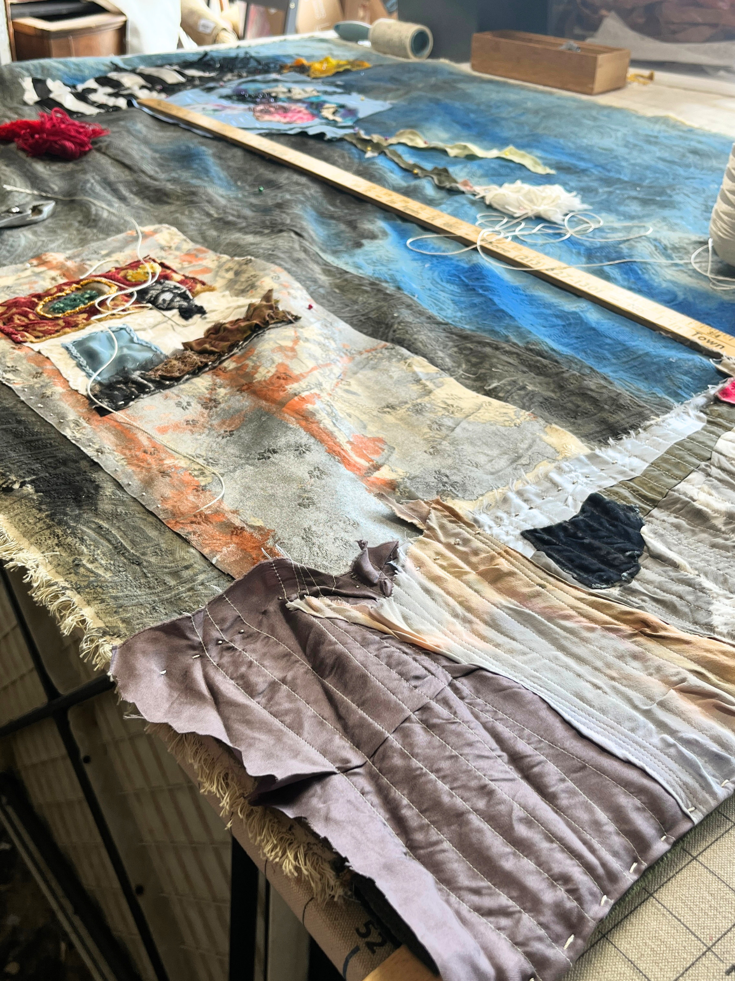 Textile art piece with various fabrics and threads on a table.