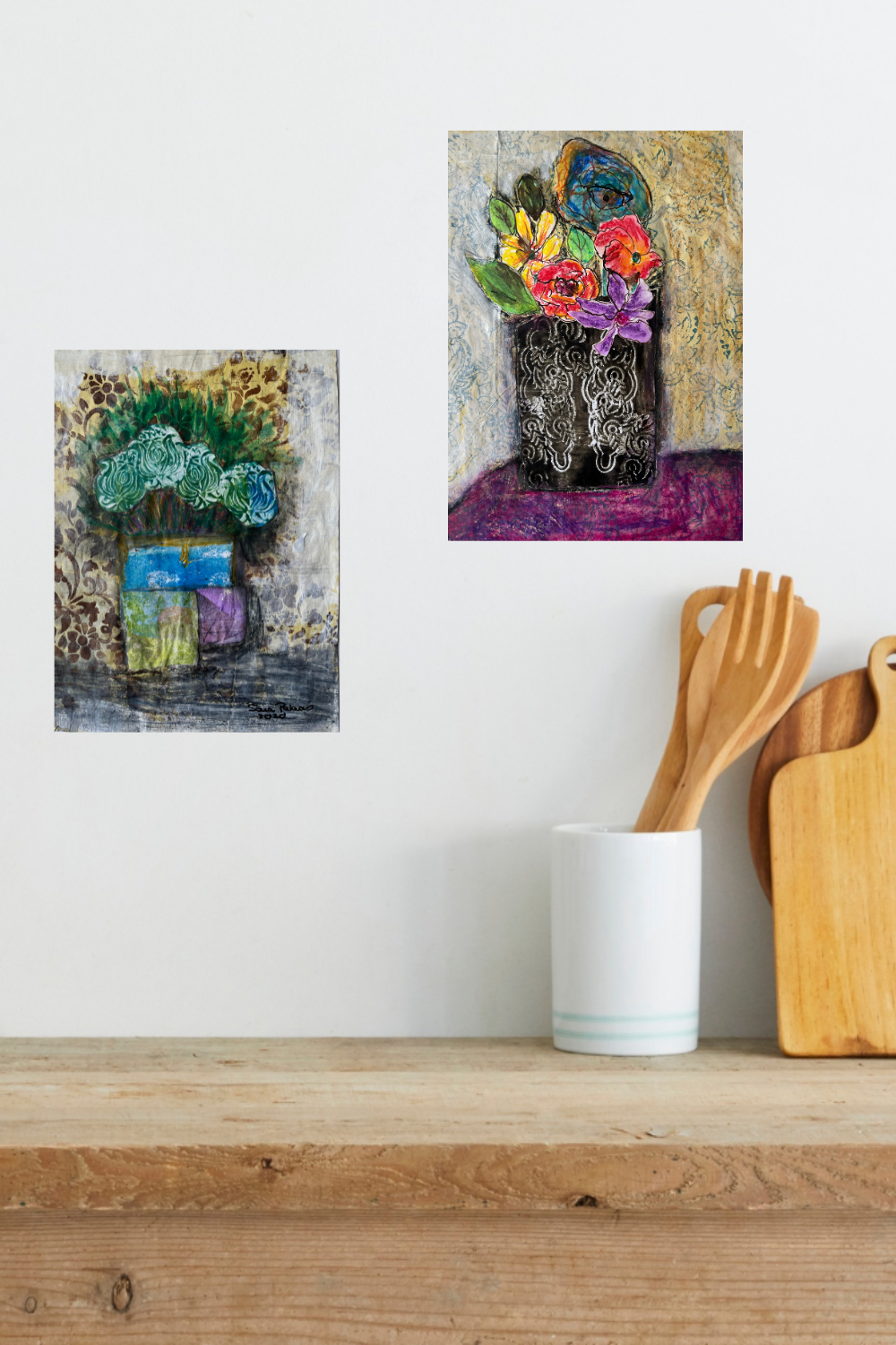 Two abstract art pieces on a wall above a wooden shelf with kitchen utensils.