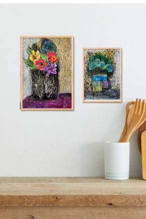 Two framed artworks of floral arrangements on a wall above a wooden shelf with kitchen utensils.