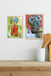 Two framed abstract artworks on a wall above a wooden shelf with kitchen utensils.