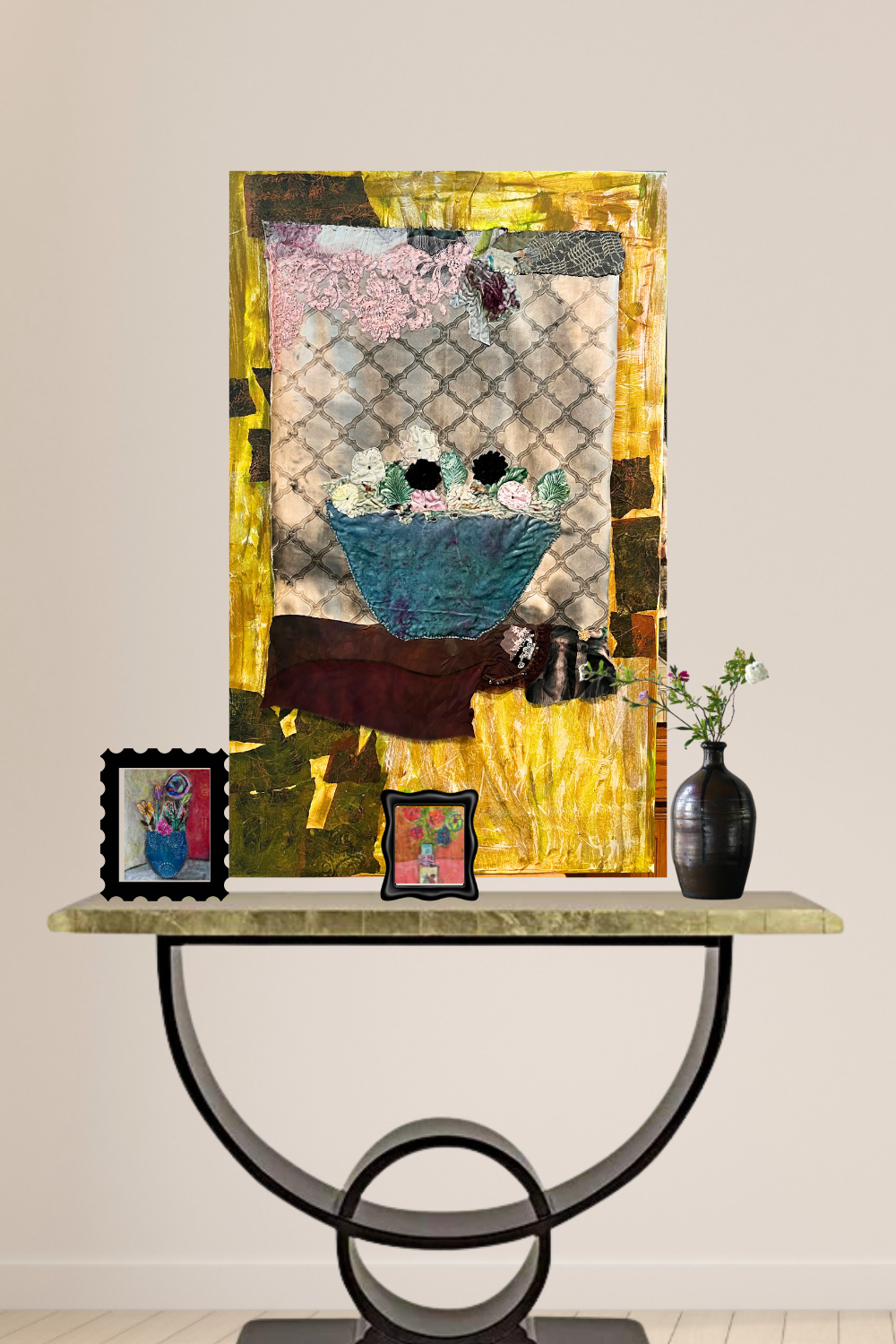 A colorful abstract still life painting of a blue bowl of flowers hangs on a beige wall above a console table styled with two small framed pictures and a black vase.