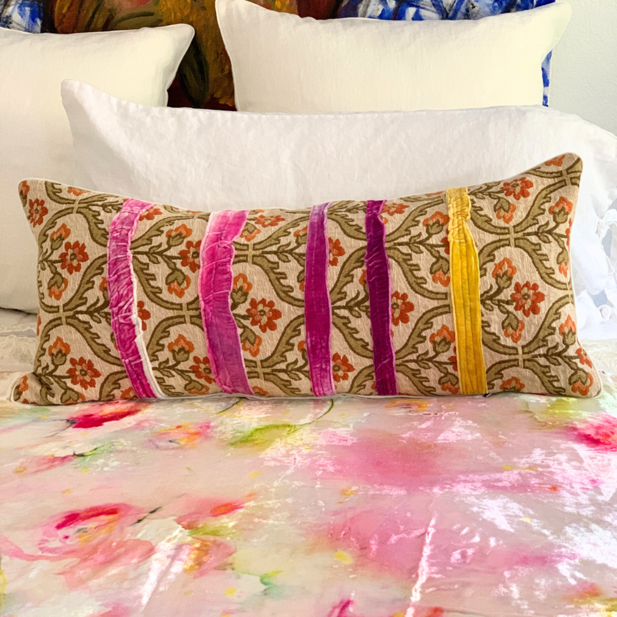 Decorative pillow with floral patterns and colorful stripes on a bed with a floral comforter.