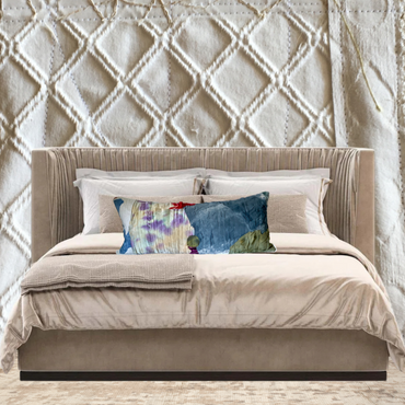 Beige upholstered bed with colorful pillows against a textured wall.