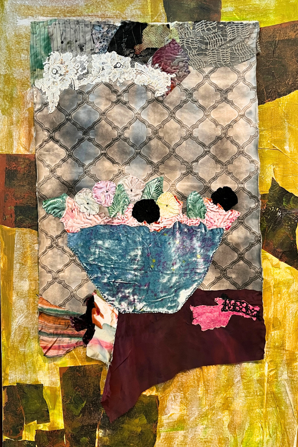 A mixed-media collage artwork featuring a blue cup or bowl with pink and green floral elements, layered over a gray patterned background and surrounded by textured yellow, brown, and green abstract patches.