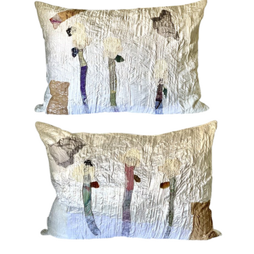 Two pillows with artistic designs of people and trees on a white background