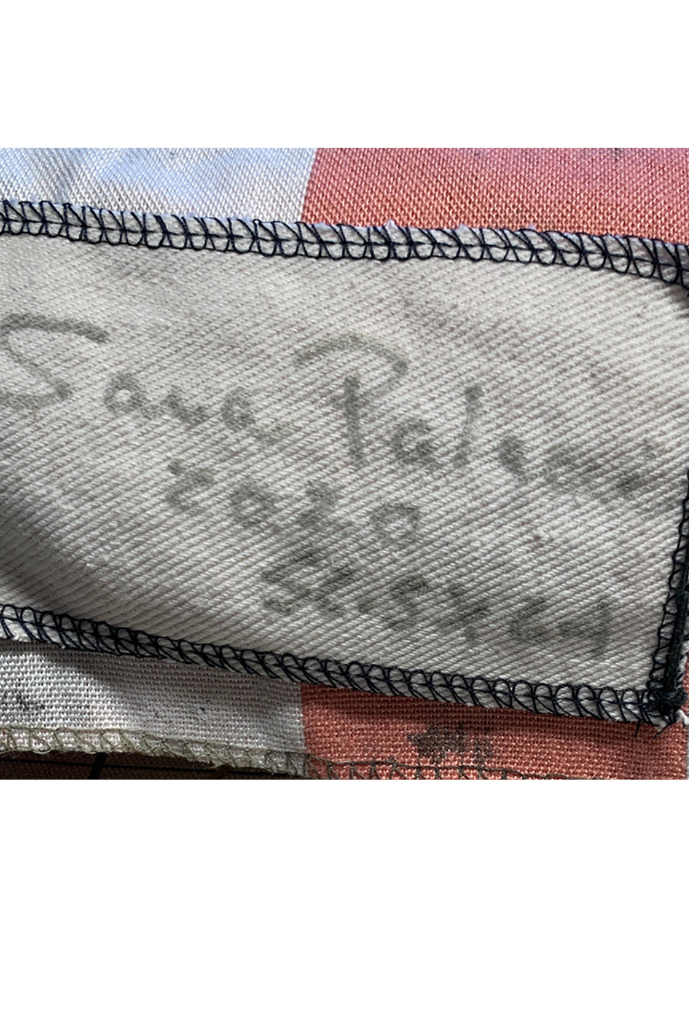 Close-up of a fabric label sewn onto a woven textile, with handwritten text reading 'Sara Palermo 2020 35.5 x 64' and black stitched border.