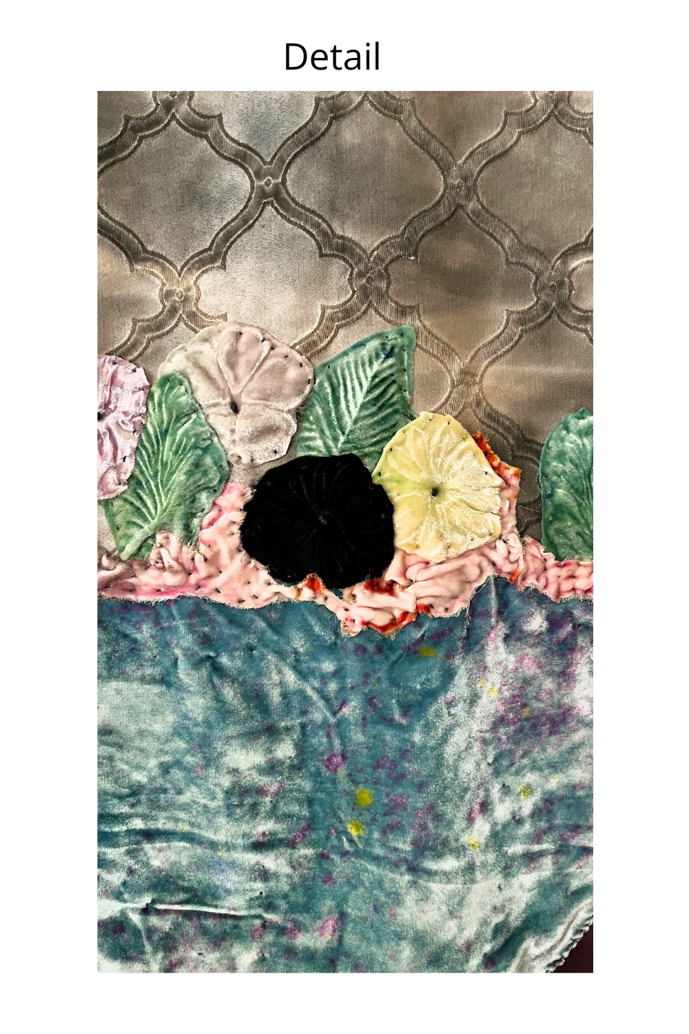 A close-up detail shot of a textured fabric item, likely a quilt or blanket, featuring a floral applique border with green, yellow, pink, and black fabric flowers against a gray trellis background, with the word 'Detail' printed at the top.