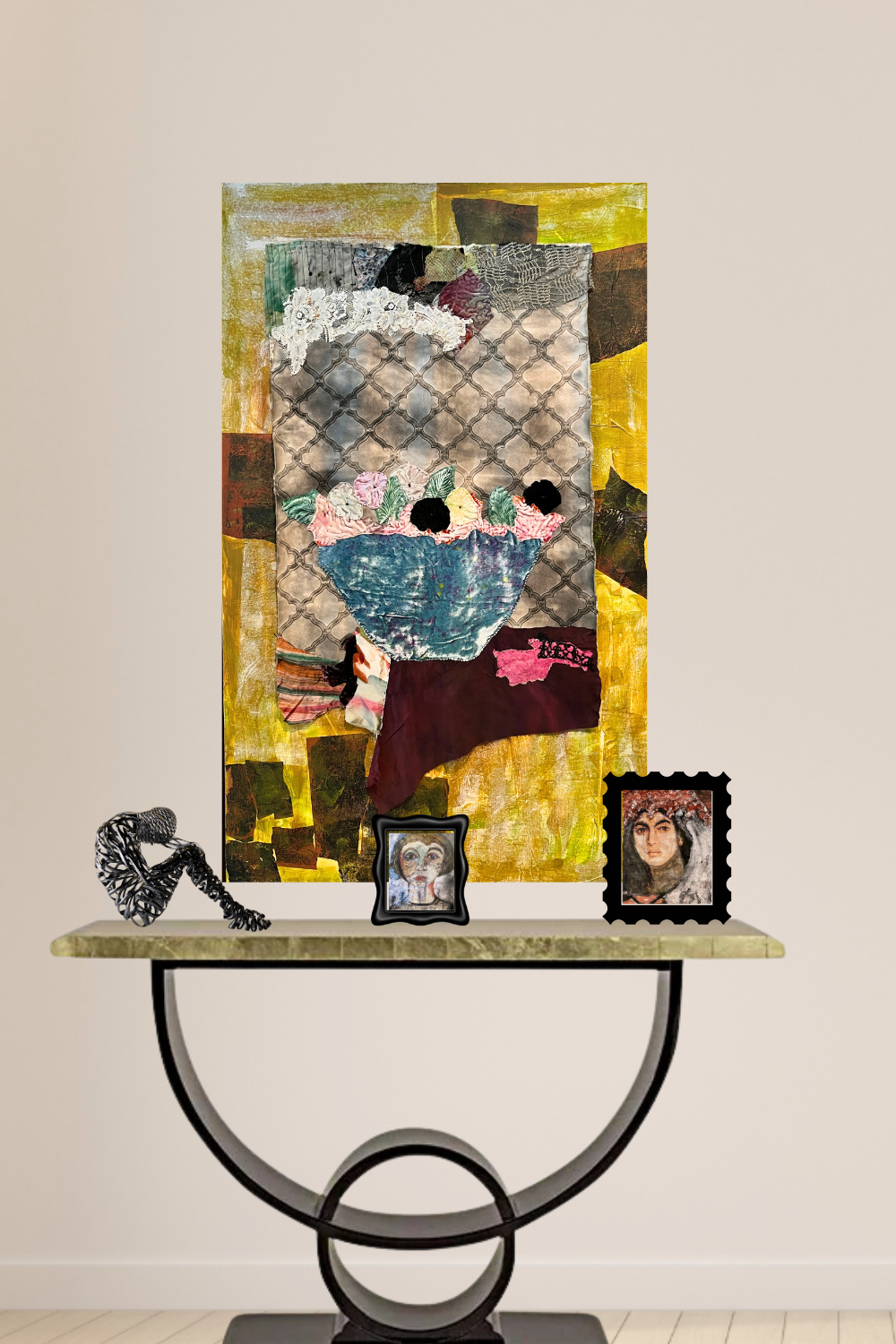 A mixed-media collage painting of a woman in a blue dress, displayed on a console table with two small framed portraits and a decorative sculpture against a beige wall.