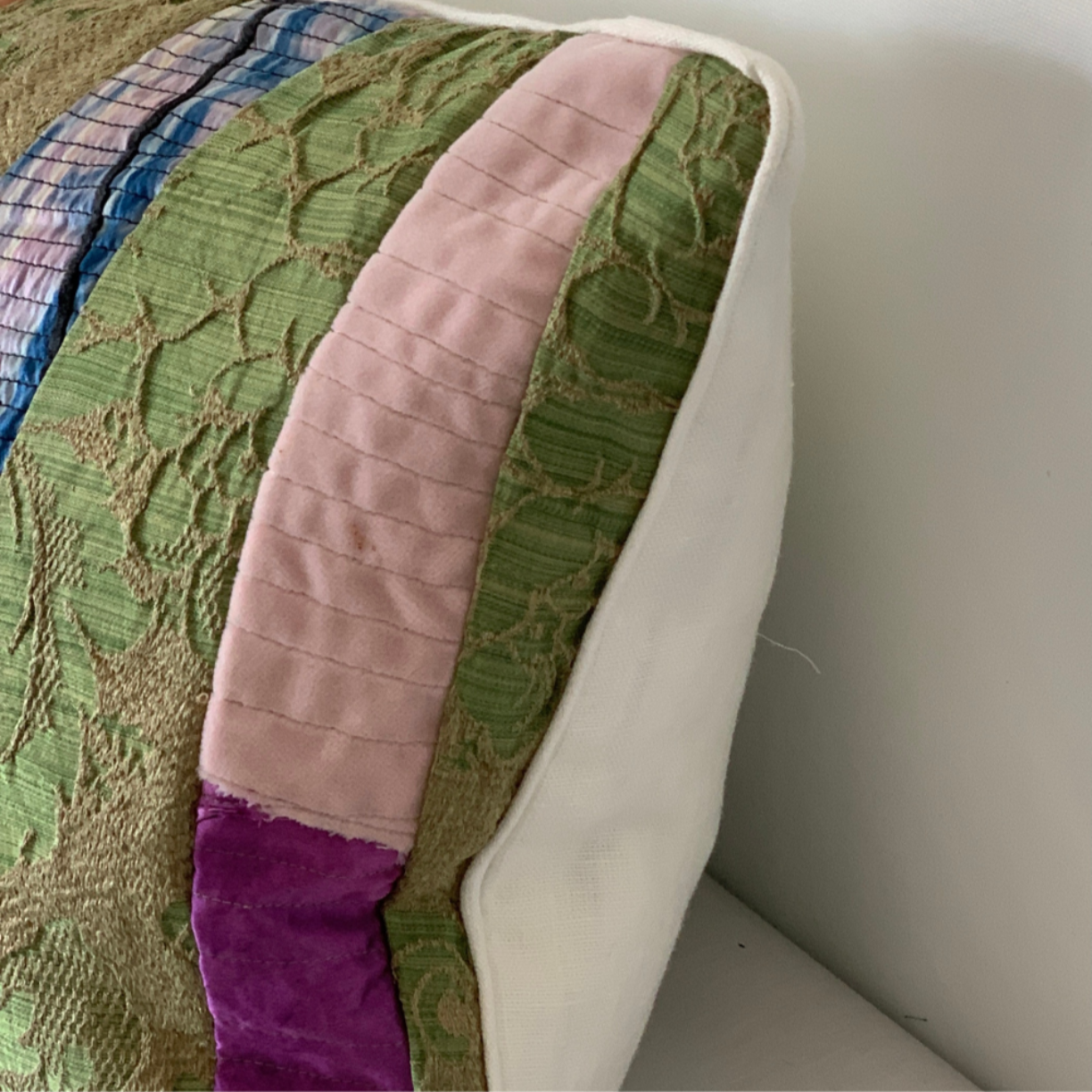 Close-up of a textured fabric with green, pink, and purple patterns on a neutral background.