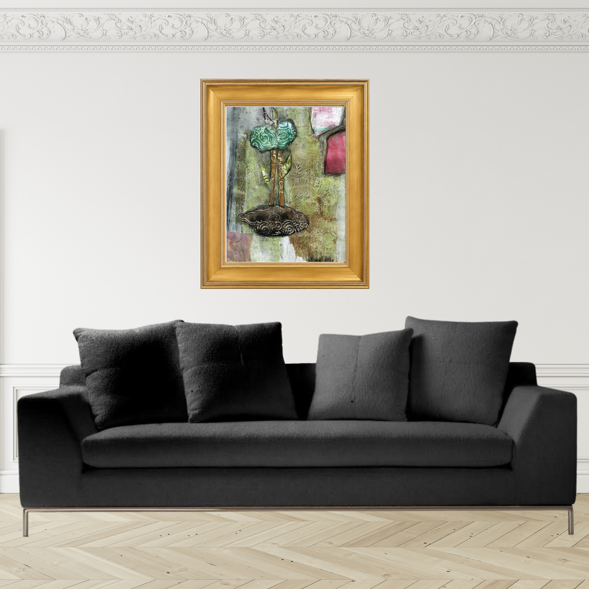 Mixed media collage titled Hay Moon by Sara Palacios. The piece features a stylized green flower with rose-like patterns, two tall stems, and layered leaves growing from a textured brown base. Surrounded by an abstract background of green, gray, and pink tones, the artwork blends organic and ornamental elements for a dreamy, earthy composition. Framed in a gold frame, on top of a sofa.