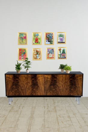 Wooden sideboard with decorative plants and framed artwork on a white wall.