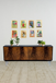 Wooden sideboard with decorative plants and framed artwork on a white wall.