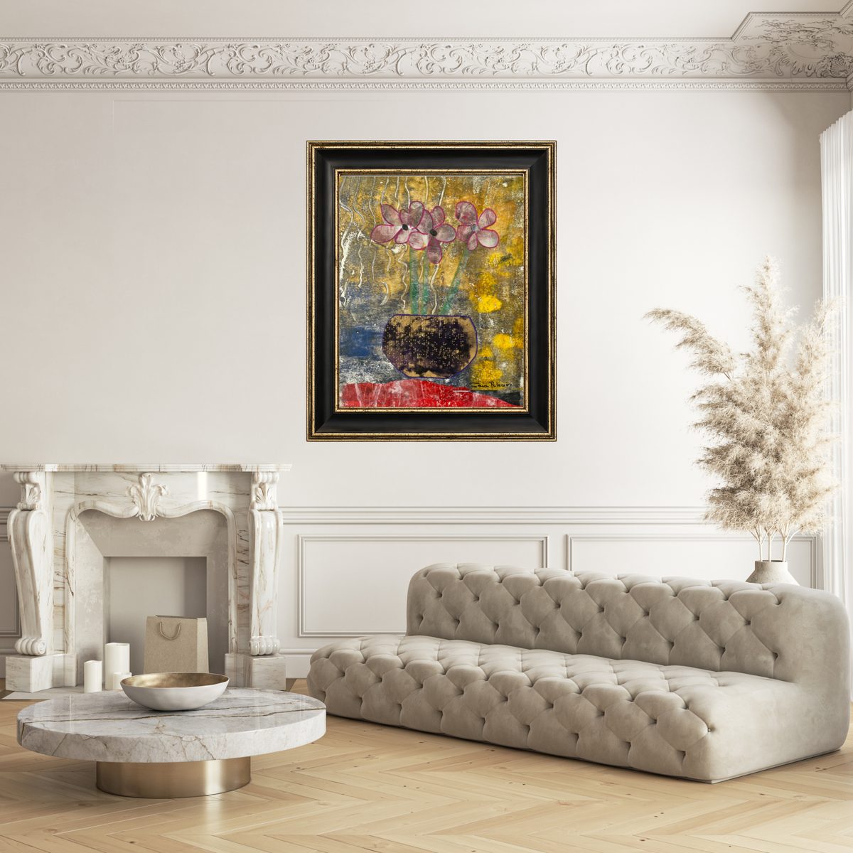 A framed abstract painting featuring pink flowers in a dark vase against a textured yellow, gold, blue, and red background, enclosed in a black frame with gold detailing. In a white living room.